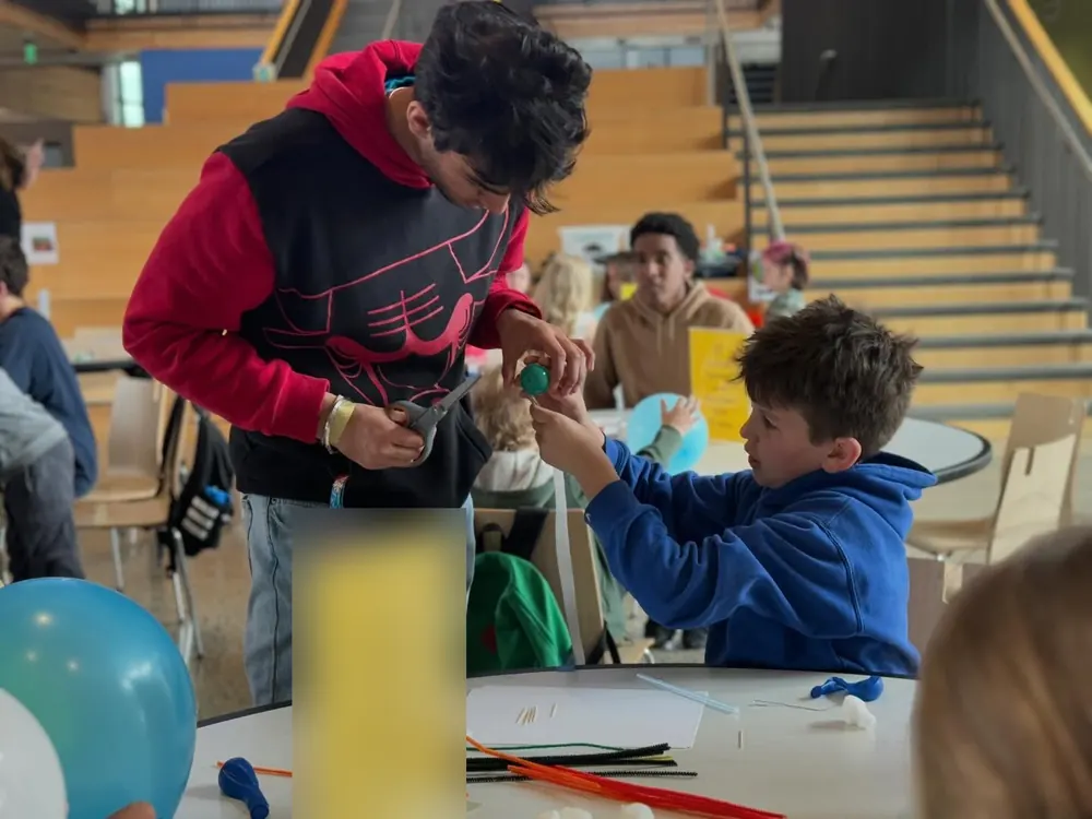 A student leader helping a young student assemble a balloon project