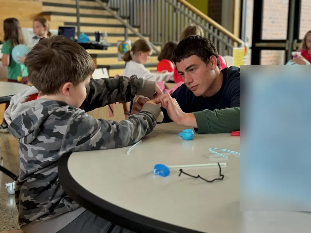 A student leader helping a young student with a pipe-cleaner build